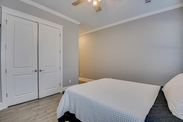 bedroom featuring visible vents, a ceiling fan, crown molding, light wood-type flooring, and a closet