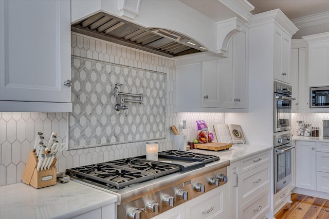 kitchen with white cabinetry, custom exhaust hood, stainless steel appliances, and ornamental molding