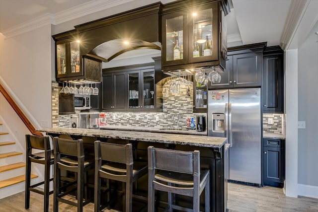 bar featuring light wood-style flooring, indoor bar, ornamental molding, backsplash, and stainless steel fridge