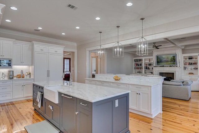 kitchen with ornamental molding, open floor plan, a center island with sink, and a sink