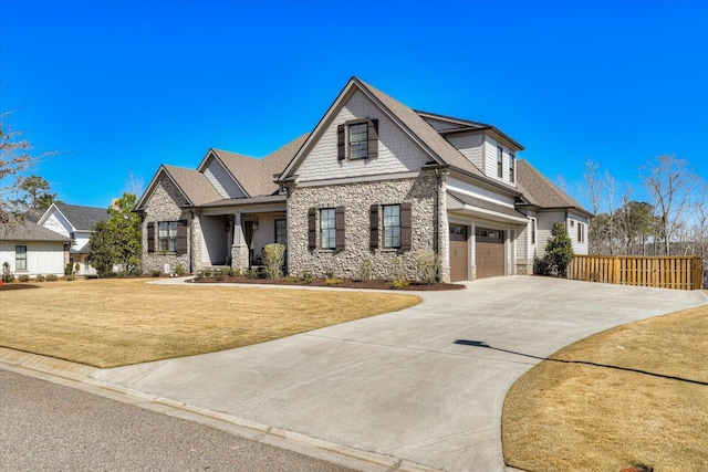 view of front of house with stone siding, a front yard, concrete driveway, and fence