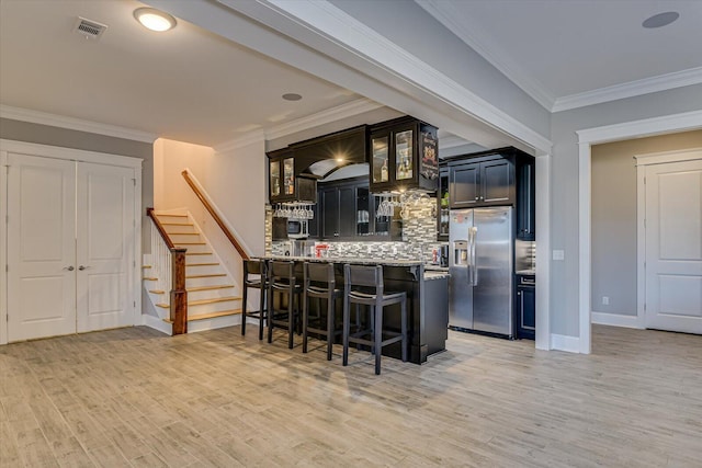 kitchen with visible vents, backsplash, stainless steel fridge, a peninsula, and a kitchen breakfast bar