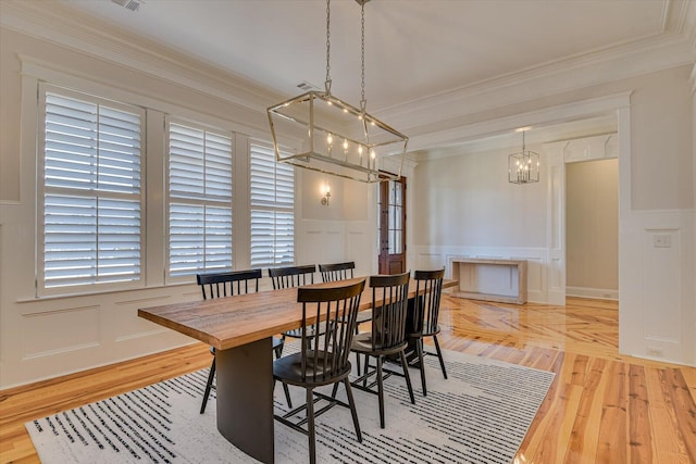 dining area with crown molding, a wainscoted wall, a decorative wall, and wood finished floors