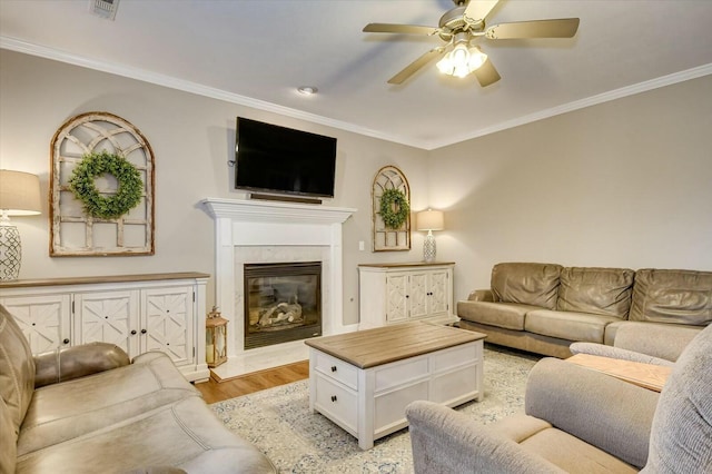 living room with crown molding, ceiling fan, a premium fireplace, and light hardwood / wood-style floors