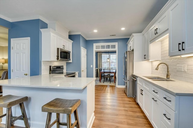 kitchen featuring sink, appliances with stainless steel finishes, white cabinetry, a kitchen bar, and kitchen peninsula