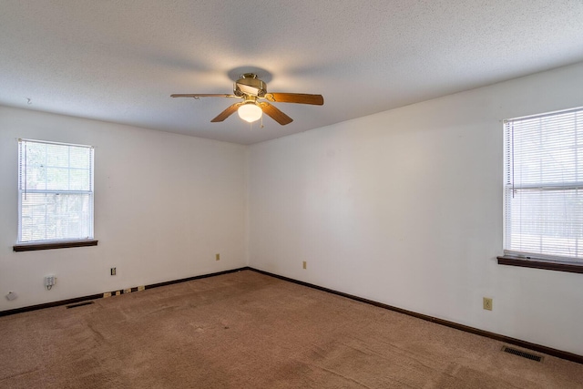 carpeted spare room with plenty of natural light, visible vents, and ceiling fan