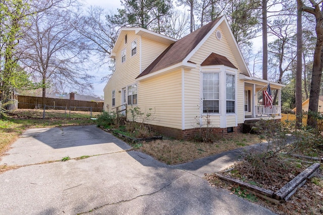 view of side of property featuring covered porch, driveway, roof with shingles, and fence