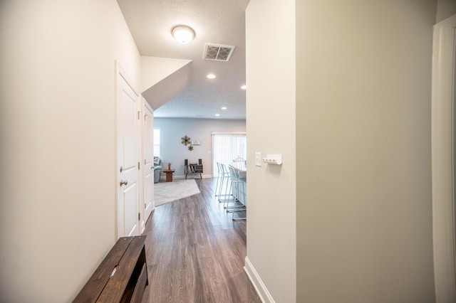 hallway featuring a textured ceiling, recessed lighting, wood finished floors, visible vents, and baseboards