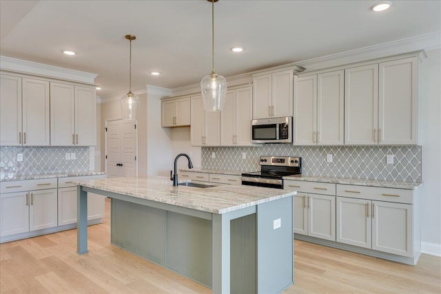 kitchen featuring sink, appliances with stainless steel finishes, hanging light fixtures, light stone counters, and an island with sink