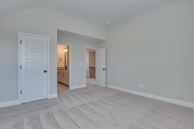 unfurnished bedroom with ensuite bath, lofted ceiling, and light carpet