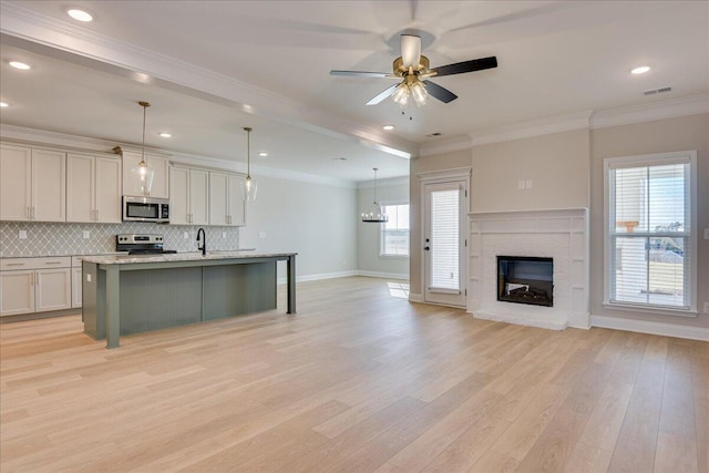 kitchen with a kitchen bar, decorative light fixtures, appliances with stainless steel finishes, light stone countertops, and a kitchen island with sink