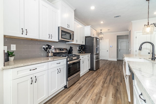 kitchen with crown molding, white cabinetry, stainless steel appliances, light stone counters, and decorative light fixtures