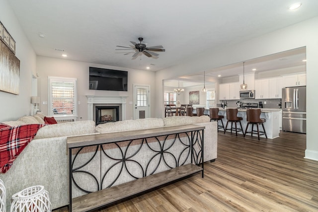 living room featuring ceiling fan with notable chandelier and light hardwood / wood-style flooring