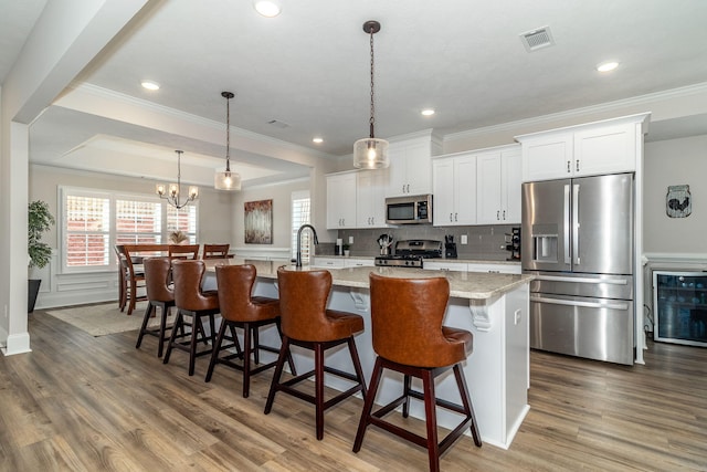 kitchen featuring appliances with stainless steel finishes, hanging light fixtures, an island with sink, white cabinets, and a kitchen bar