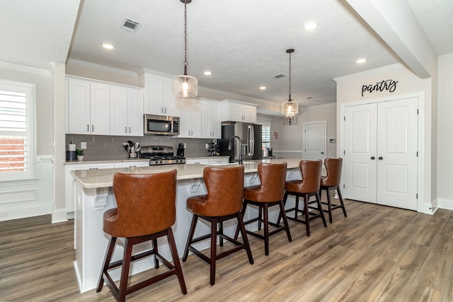 kitchen featuring white cabinetry, hanging light fixtures, stainless steel appliances, a spacious island, and a kitchen bar