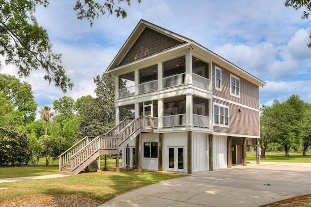 raised beach house featuring stairs, a front yard, concrete driveway, a balcony, and french doors