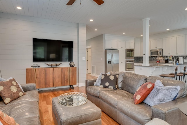 living room featuring wood walls, a ceiling fan, light wood-type flooring, ornate columns, and visible vents