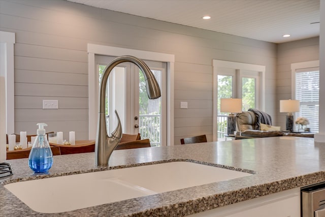 kitchen featuring light stone countertops, a sink, wood walls, recessed lighting, and open floor plan