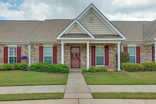 view of front of house with stone siding, a shingled roof, and a front yard
