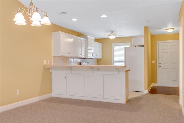 kitchen featuring freestanding refrigerator, a peninsula, light carpet, light countertops, and white cabinetry