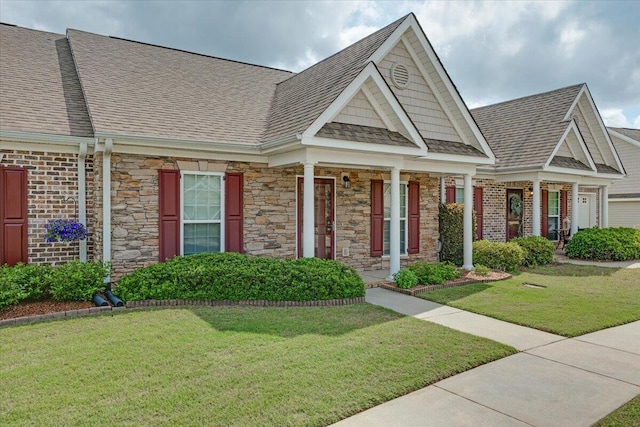view of front of house with roof with shingles, stone siding, a front yard, and covered porch