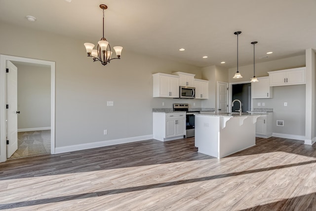 kitchen with stainless steel appliances, white cabinetry, baseboards, and wood finished floors