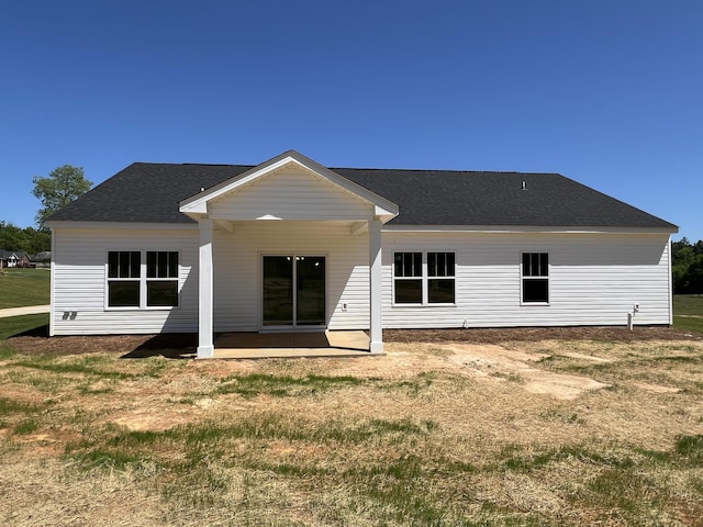 back of property with a yard, roof with shingles, and a patio