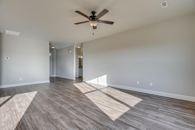 empty room featuring ceiling fan, wood finished floors, visible vents, and baseboards