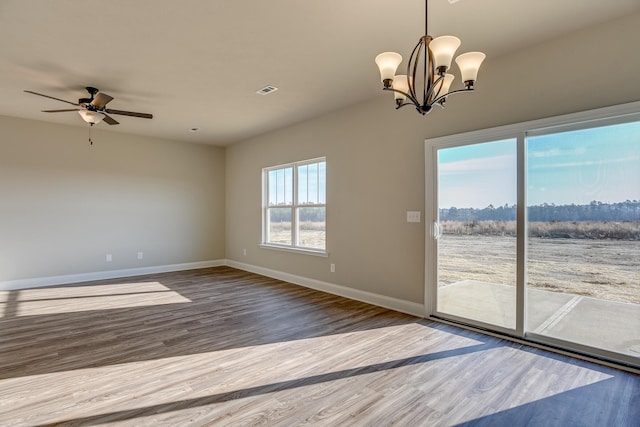 empty room with ceiling fan with notable chandelier, visible vents, baseboards, and wood finished floors