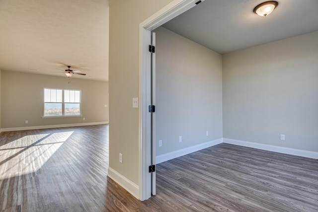 empty room featuring a ceiling fan, dark wood-style flooring, and baseboards