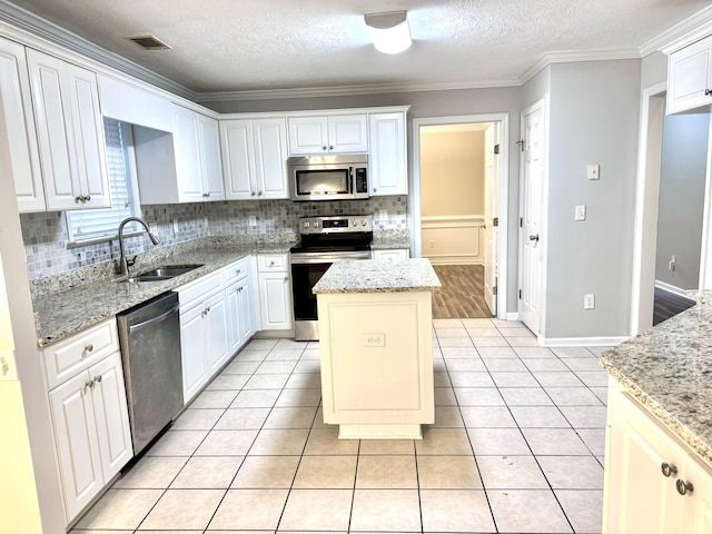 kitchen with sink, light stone countertops, appliances with stainless steel finishes, a kitchen island, and white cabinetry