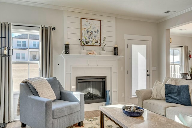 living room featuring a tile fireplace, ornamental molding, and light hardwood / wood-style floors