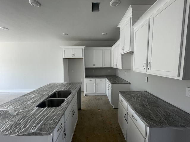 kitchen with dark stone countertops, a sink, a kitchen island with sink, and white cabinets