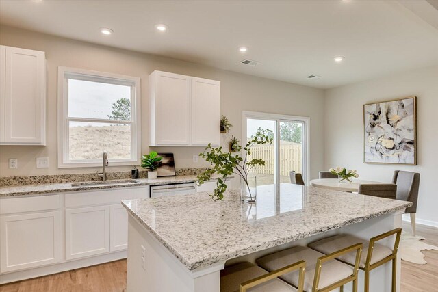 kitchen featuring white cabinetry, sink, a kitchen breakfast bar, light hardwood / wood-style flooring, and a kitchen island