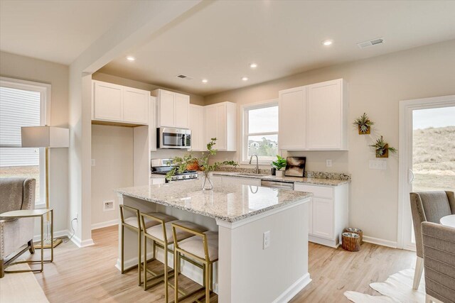 kitchen featuring light wood-type flooring, light stone counters, stainless steel appliances, white cabinetry, and a kitchen island