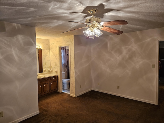 unfurnished bedroom with ensuite bath, ceiling fan, sink, and dark colored carpet