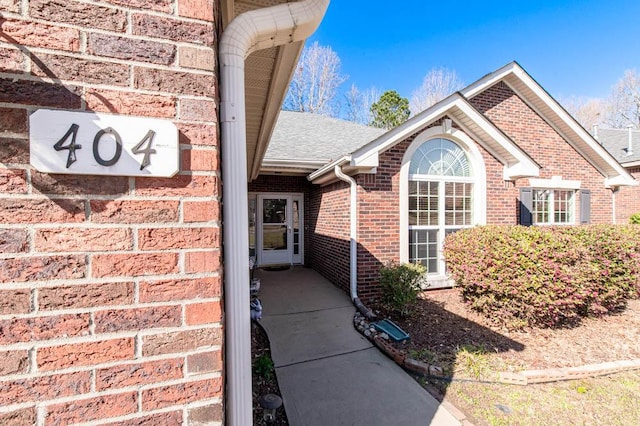 entrance to property featuring brick siding and roof with shingles