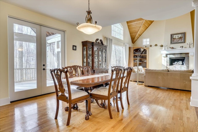 dining space featuring light hardwood / wood-style floors, wooden ceiling, a tiled fireplace, french doors, and lofted ceiling with beams