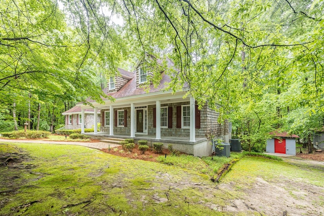 cape cod house with central AC, covered porch, a front yard, and a storage unit