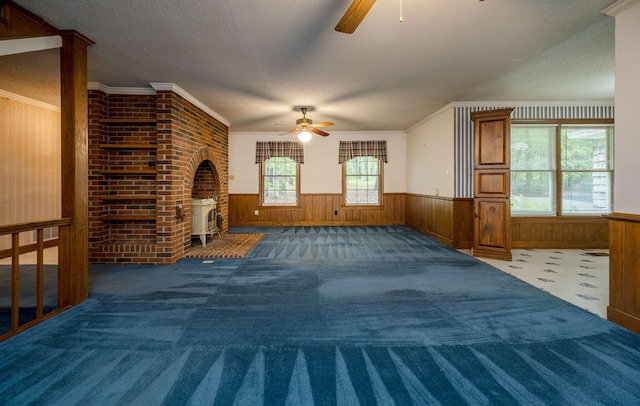 unfurnished living room featuring a textured ceiling, a wood stove, ceiling fan, and ornamental molding