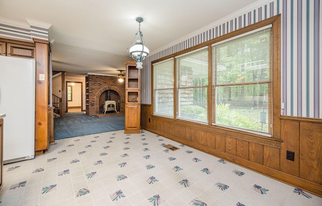 unfurnished living room with wood walls, a wood stove, and crown molding