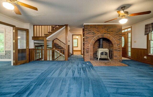 unfurnished living room with a wood stove, wood walls, plenty of natural light, and ornamental molding