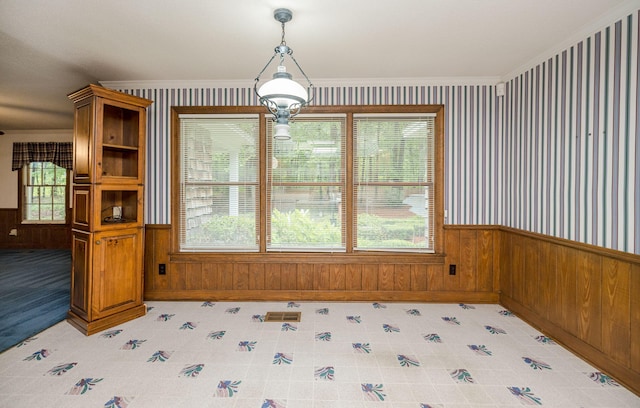 unfurnished dining area featuring crown molding, a healthy amount of sunlight, and wood walls