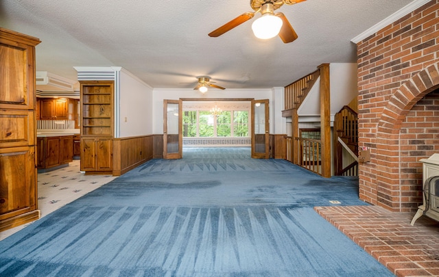 unfurnished living room featuring a textured ceiling, ceiling fan, crown molding, a wood stove, and wood walls