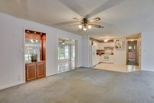 unfurnished living room featuring a textured ceiling, ceiling fan with notable chandelier, wood walls, and light carpet