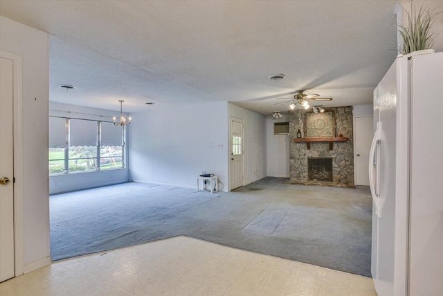 unfurnished living room with a textured ceiling, ceiling fan with notable chandelier, a stone fireplace, and light carpet