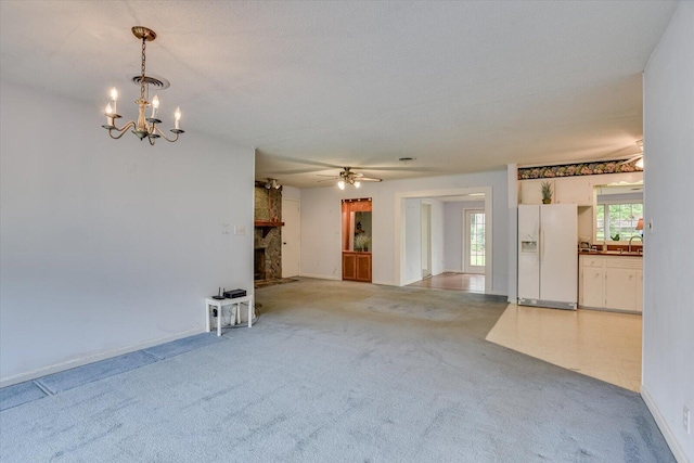 unfurnished living room featuring ceiling fan with notable chandelier, a stone fireplace, light colored carpet, and a textured ceiling