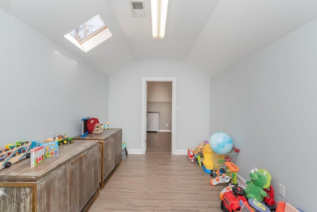 playroom featuring lofted ceiling with skylight, baseboards, visible vents, and light wood-type flooring