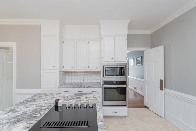 kitchen with light stone countertops, stainless steel appliances, wainscoting, white cabinetry, and crown molding