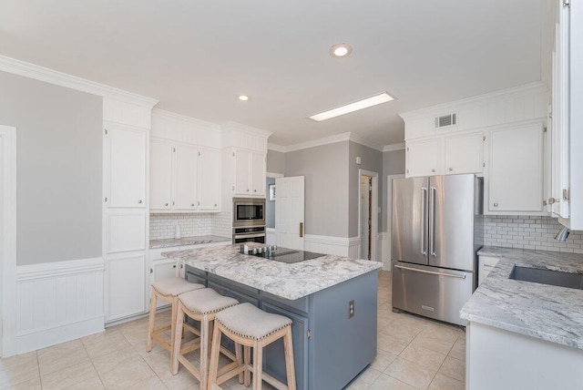 kitchen featuring a wainscoted wall, a sink, a center island, white cabinetry, and appliances with stainless steel finishes